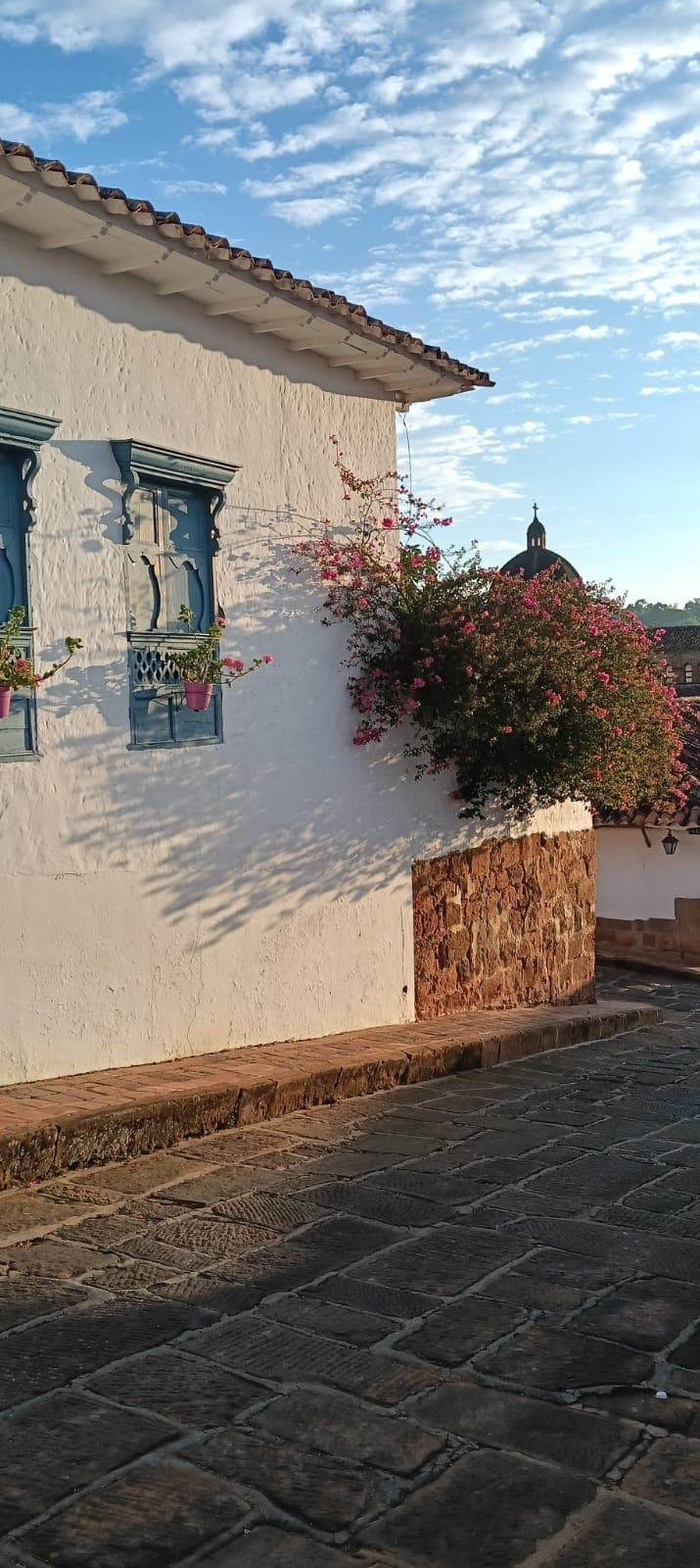 Buganvilla fucsia desbordándose en una esquina colonial de Barichara con cúpula de iglesia al fondo